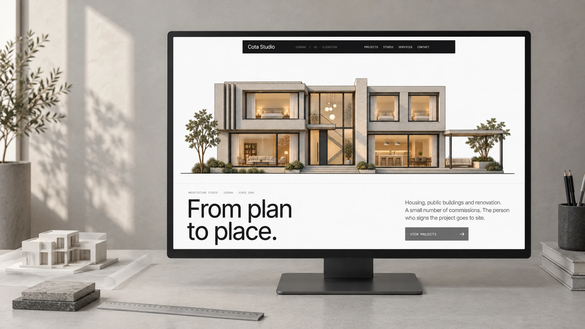 Cota Studio on a large monitor in a pearl-grey architecture atelier, beside a white massing model, tracing paper and material samples.